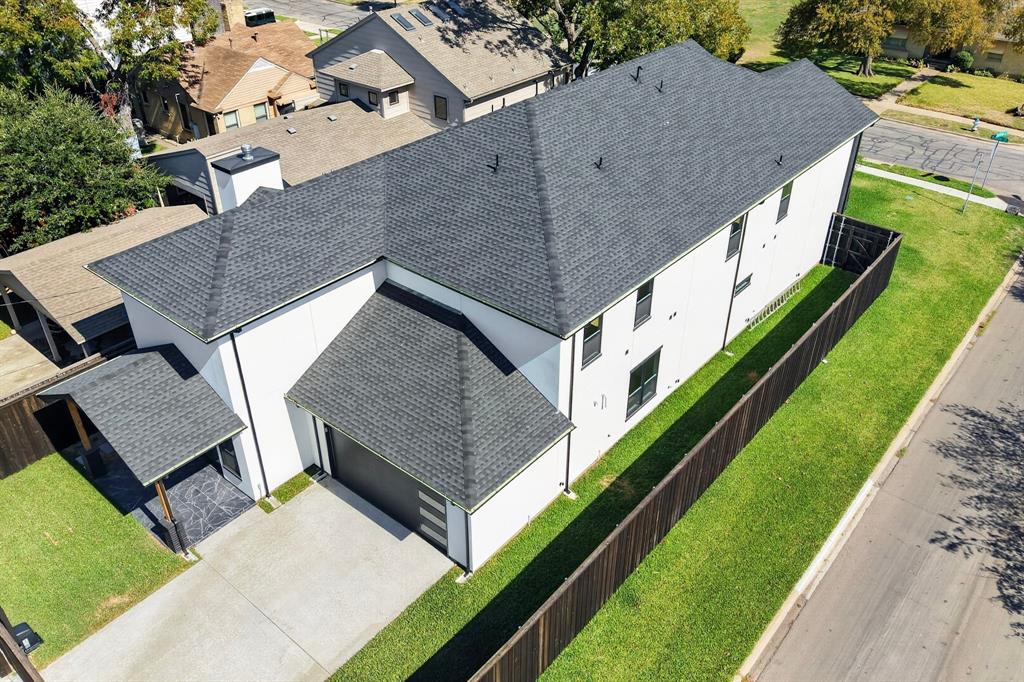 Exterior profile featuring a white facade, dark architectural shingle roof, attached garage with a multi-panel door, and a fenced yard with a concrete driveway