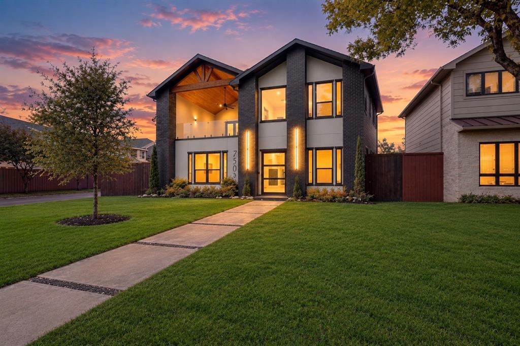 Modern two-story exterior featuring dark brick masonry, wood-accented vaulted balcony, glass railing, and linear wall-mounted exterior lighting Modern two-story exterior featuring dark brick masonry, wood-accented vaulted balcony, glass railing, and linear wall-mounted exterior lighting