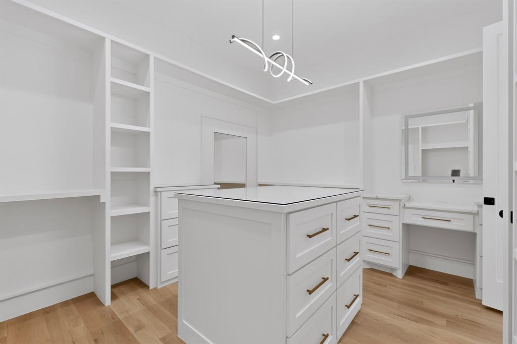 Custom walk-in closet featuring floor-to-ceiling built-in shelving, a central island with soft-close drawers, a dedicated vanity station, wood-finish flooring, and contemporary pendant lighting