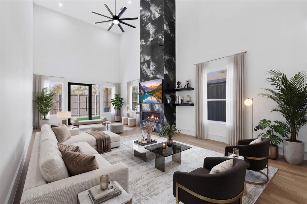 Double-height ceiling, floor-to-ceiling dark-veined stone fireplace surround, modern linear fireplace, multi-blade ceiling fan, and wood-finish flooring Double-height ceiling, floor-to-ceiling dark-veined stone fireplace surround, modern linear fireplace, multi-blade ceiling fan, and wood-finish flooring