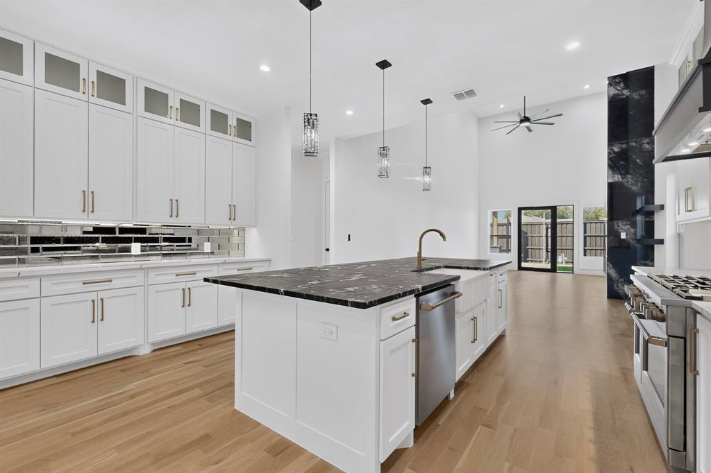 Kitchen featuring floor-to-ceiling white cabinetry, a center island with a dark stone countertop, apron-front sink, wood-finish flooring, and high-vaulted ceilings