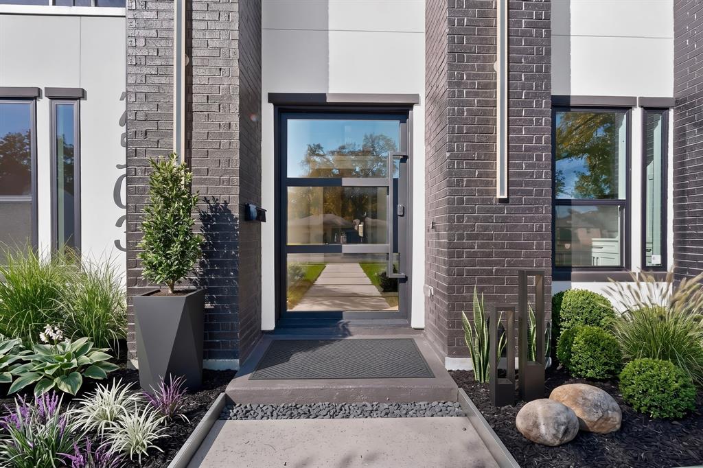 Modern entryway featuring dark brick masonry, a glass-paneled door with a geometric steel handle, vertical accent lighting, and concrete steps with black river rock detailing Modern entryway featuring dark brick masonry, a glass-paneled door with a geometric steel handle, vertical accent lighting, and concrete steps with black river rock detailing