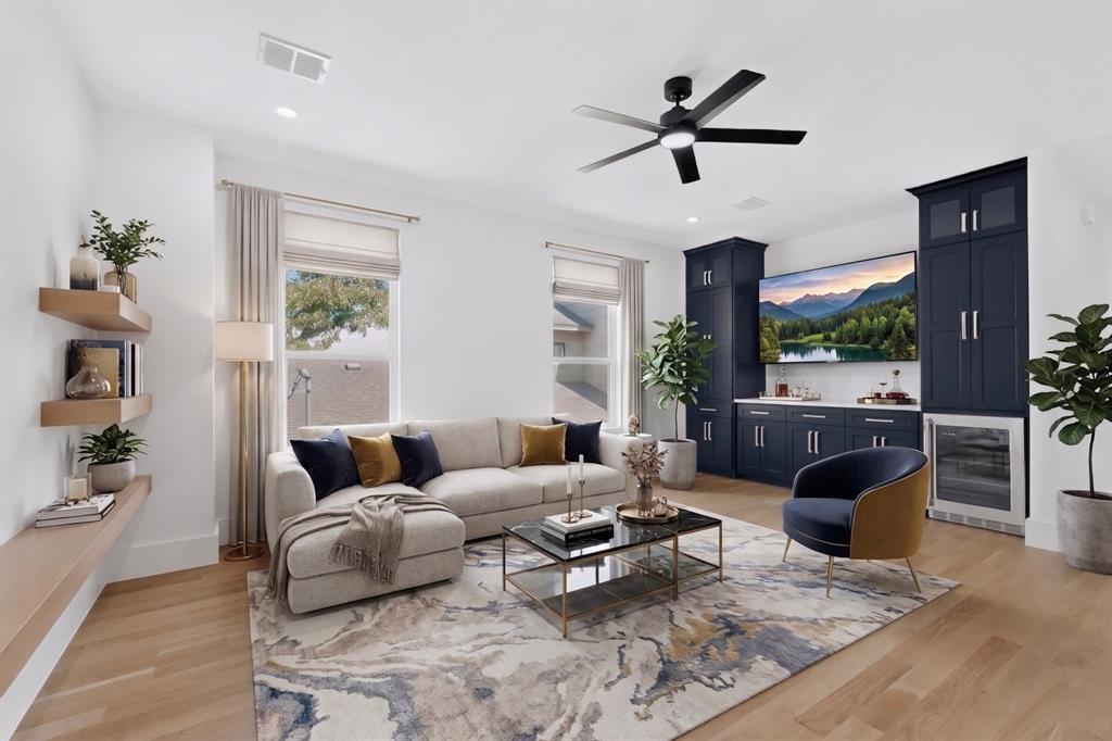 Living space featuring wood-finish flooring, custom dark cabinetry with integrated beverage refrigerator, wall-mounted floating shelves, and a ceiling fan with light fixture