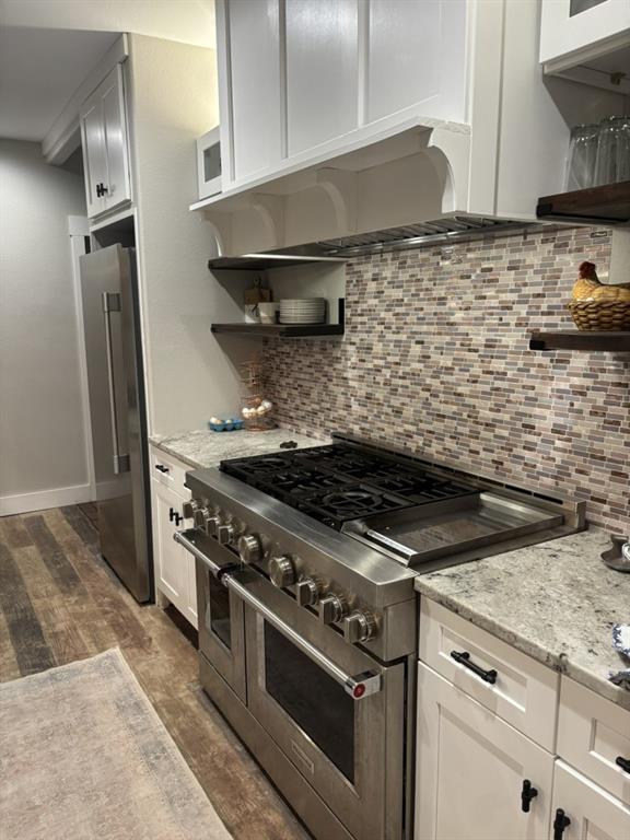 Kitchen featuring a professional-grade stainless steel range with a built-in griddle, white shaker-style cabinetry, mosaic tile backsplash, stone-finish countertops, and wood-finish flooring