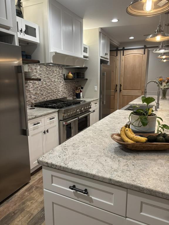 Kitchen featuring white shaker-style cabinetry, stone countertops, stainless steel professional-grade range, mosaic tile backsplash, and wood-finish flooring