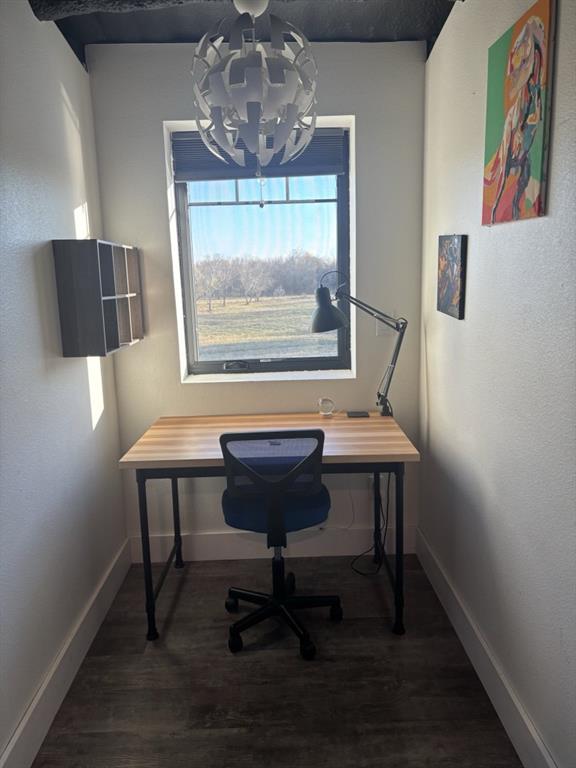 Room featuring wood-finish flooring, a centrally positioned ceiling pendant light, a recessed wall-mounted shelving unit, and a window with exterior landscape exposure