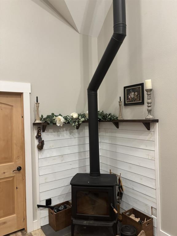 Freestanding black metal stove featuring a vertical flue, white shiplap accent wall, dark-stained floating corner shelving, and a natural wood door with matching trim