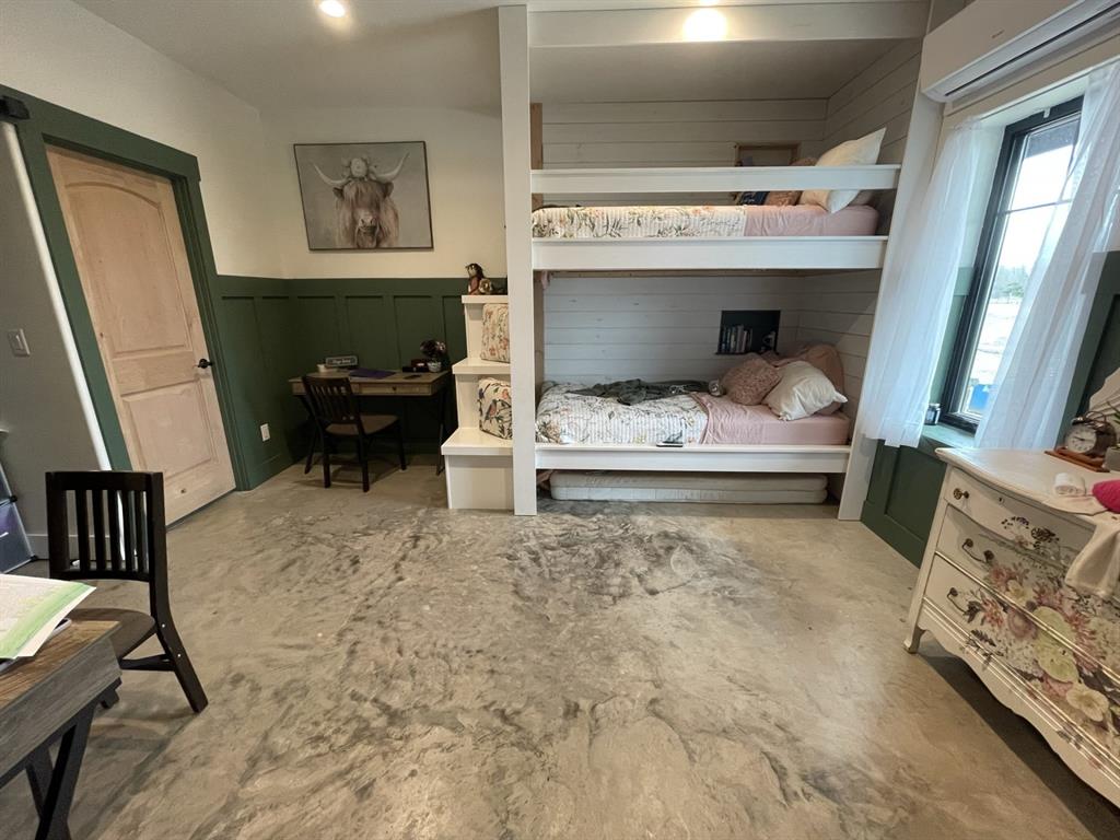 Built-in white bunk bed frame with integrated staircase, green wainscoting, smooth concrete flooring, multi-panel wood door, and recessed lighting