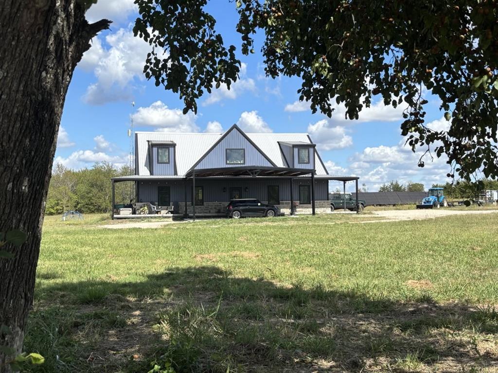 Barndominium-style exterior featuring metal siding, stone veneer accents, a standing seam metal roof, dormer windows, and an expansive covered porch Barndominium-style exterior featuring metal siding, stone veneer accents, a standing seam metal roof, dormer windows, and an expansive covered porch