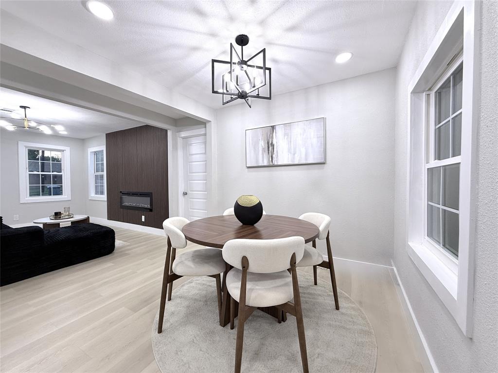 Open-concept interior featuring wood-finish flooring, a contemporary geometric chandelier, a floor-to-ceiling dark wood accent wall, and a built-in linear fireplace