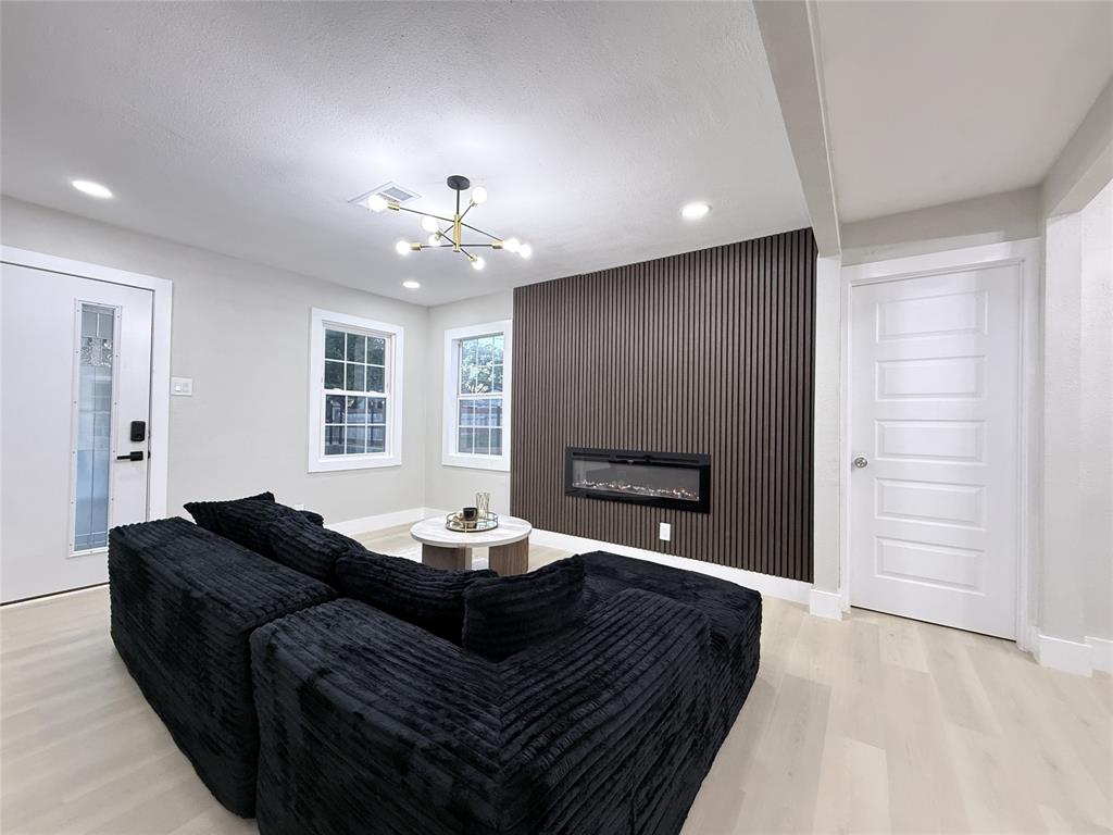 Vertical slat accent wall with a linear electric fireplace, modern multi-arm chandelier, light-toned wood-finish flooring, and multi-pane windows