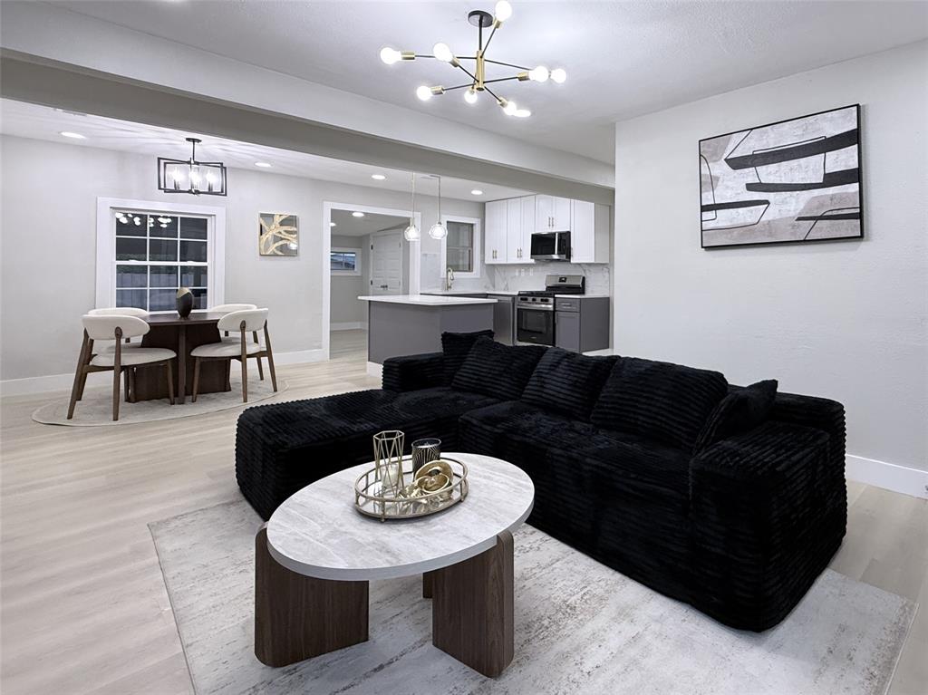 Open concept interior featuring wood-finish flooring, recessed lighting, a modern multi-arm chandelier, and a kitchen with white upper cabinetry and a center island