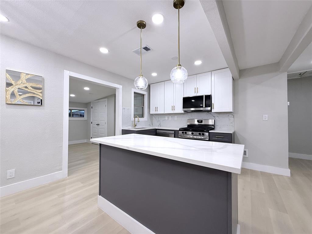 Kitchen featuring a central island with a solid surface countertop, white shaker-style cabinetry, stainless steel appliances, and dual globe pendant lighting over the workspace
