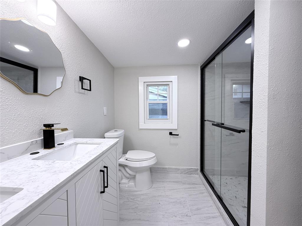 Bathroom featuring a dual-sink vanity with light stone-patterned countertops, walk-in shower with matte black fixtures and a glass enclosure, and patterned tile flooring