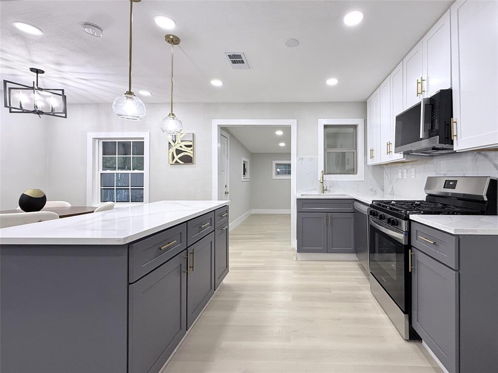 Kitchen featuring a large central island, white quartz countertops, dual-tone shaker cabinetry, wood-finish flooring, and pendant lighting