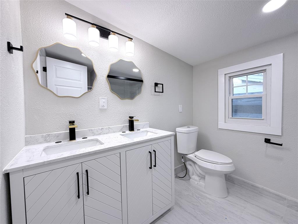 Double vanity with stone-look countertop, integrated dual sinks, chevron-patterned cabinetry, matte black hardware, and two scalloped-edge mirrors