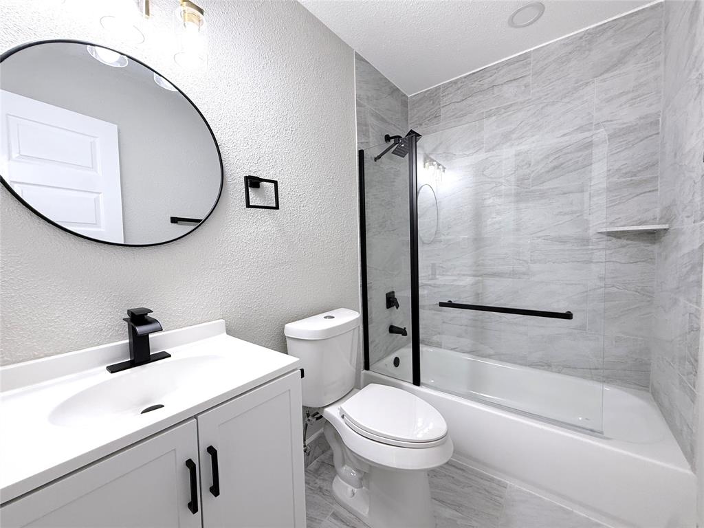 Bathroom featuring a white vanity with a matte black faucet, oval wall-mounted mirror, and a glass-enclosed shower-tub combination with horizontal tile surround and matte black fixtures