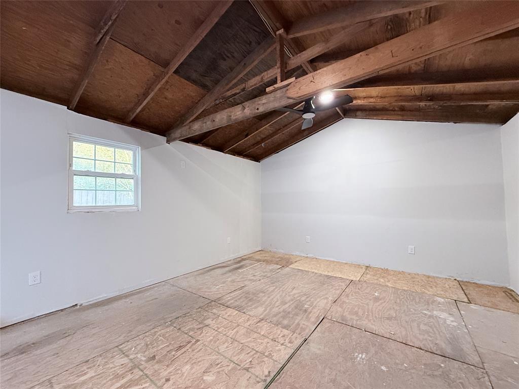Interior space featuring exposed wood-beam vaulted ceilings, paneled walls, a single-pane window, and an attached ceiling fan
