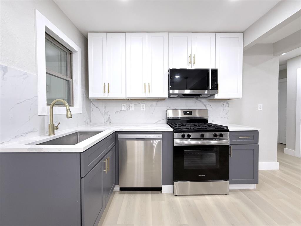 Kitchen featuring two-tone shaker cabinetry, stone-patterned backsplash, stainless steel appliances, and a gold-finish arched faucet