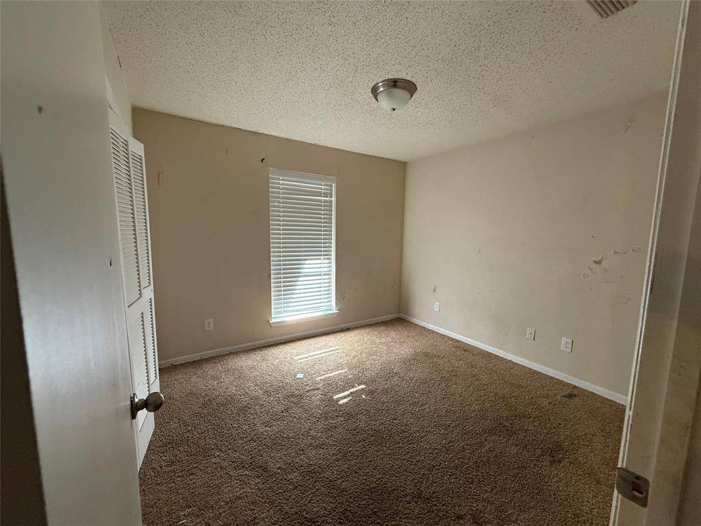 Room featuring carpeted flooring, a single window with horizontal blinds, and a built-in closet with louvered doors