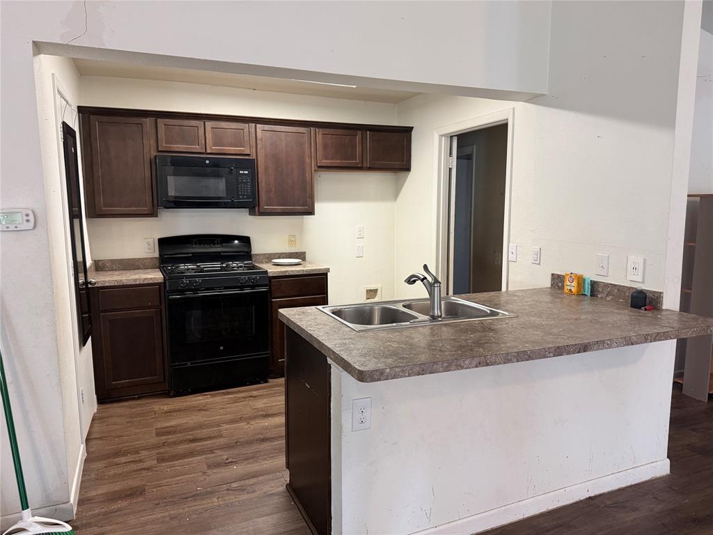 Kitchen featuring dark wood cabinetry, laminate countertops, a dual-basin stainless steel sink with a high-arch faucet, black appliance suite, and wood-finish flooring