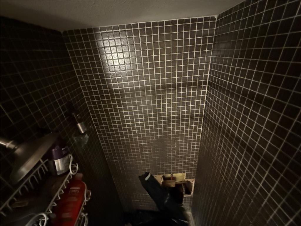 Shower surround featuring dark, square-grid mosaic wall tile and a fixed showerhead