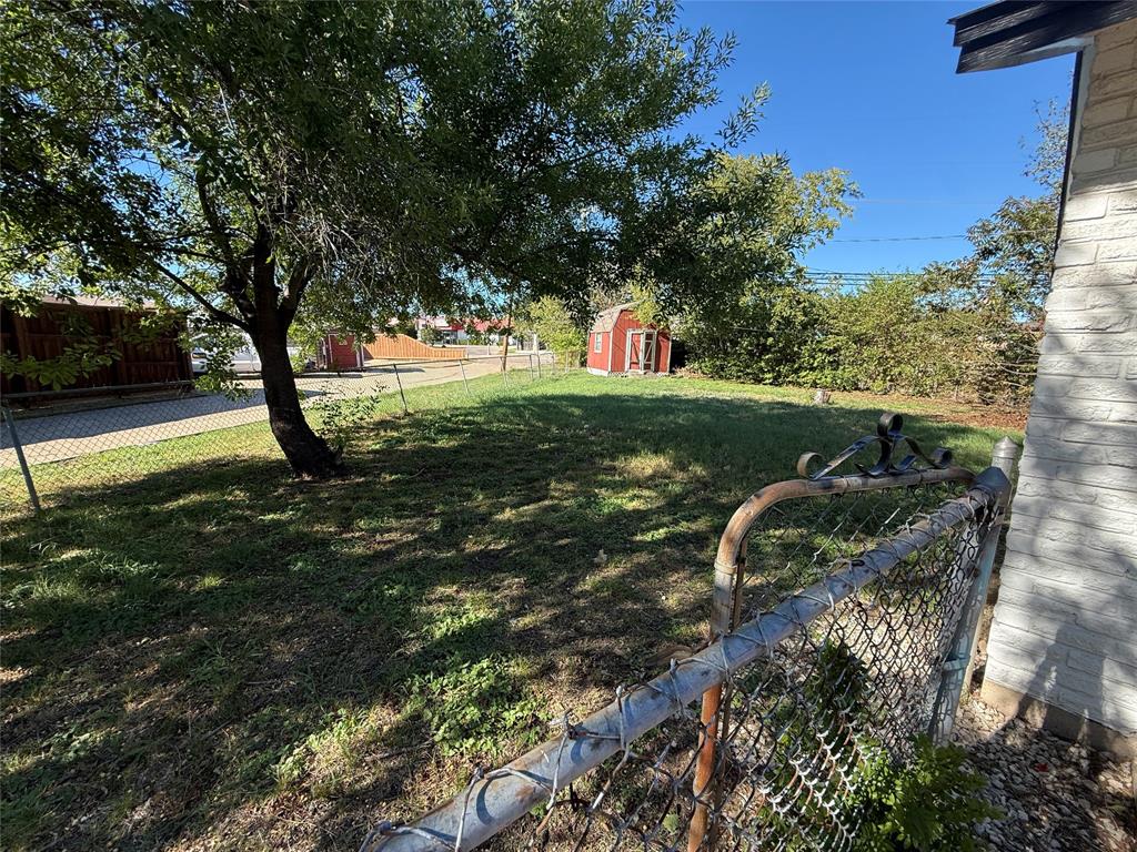 Expansive yard featuring mature trees, a chain-link fence, and a detached storage structure
