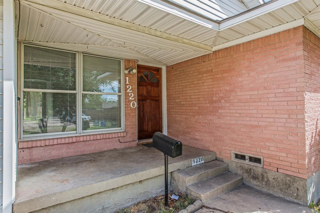 Brick facade exterior featuring a covered front porch, concrete steps, a wood-finish front door with arched glass inlay, and large multi-pane windows Brick facade exterior featuring a covered front porch, concrete steps, a wood-finish front door with arched glass inlay, and large multi-pane windows
