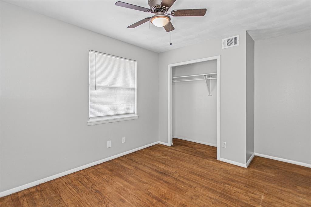 Room interior featuring wood-finish flooring, neutral wall paint, a ceiling fan with integrated lighting, and a closet with built-in shelving
