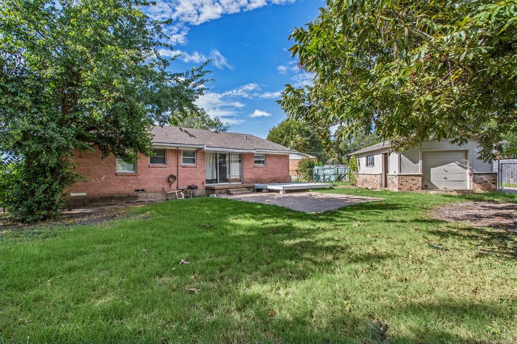 Exterior featuring brick cladding, a detached garage, a paved patio area, and mature trees on the lot