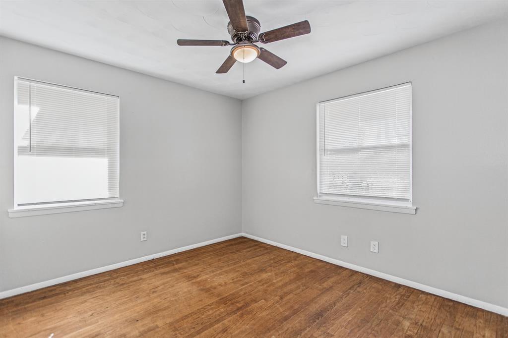 Neutral-toned interior space featuring wood-finish flooring, two dual-pane windows with integrated blinds, and a central ceiling fan with an integrated light fixture