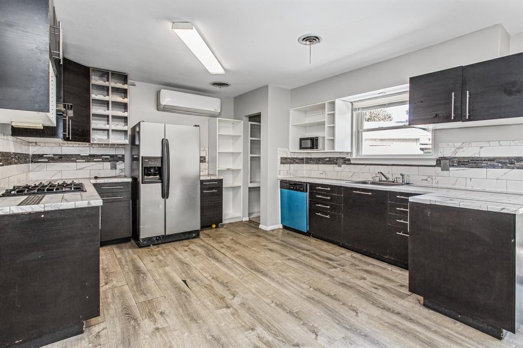 Kitchen featuring wood-finish flooring, dark cabinetry, stone-patterned countertops, a tiled backsplash, and stainless steel appliances Kitchen featuring wood-finish flooring, dark cabinetry, stone-patterned countertops, a tiled backsplash, and stainless steel appliances