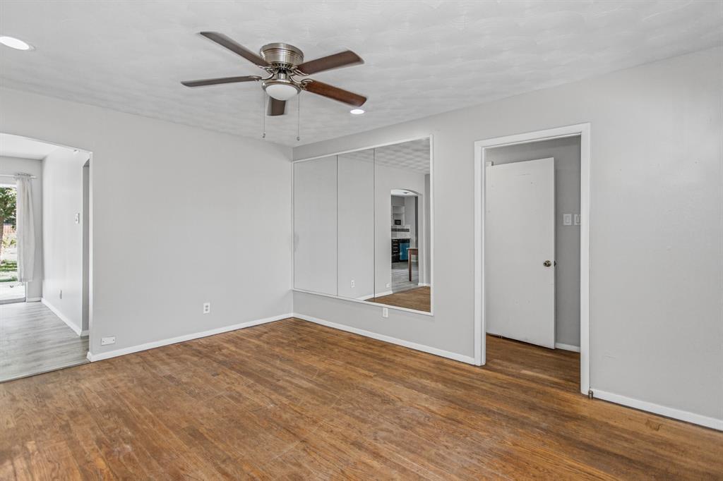 Room featuring wood-finish flooring, recessed lighting, a brushed-metal ceiling fan, and wall-to-wall mirrored closet doors Room featuring wood-finish flooring, recessed lighting, a brushed-metal ceiling fan, and wall-to-wall mirrored closet doors