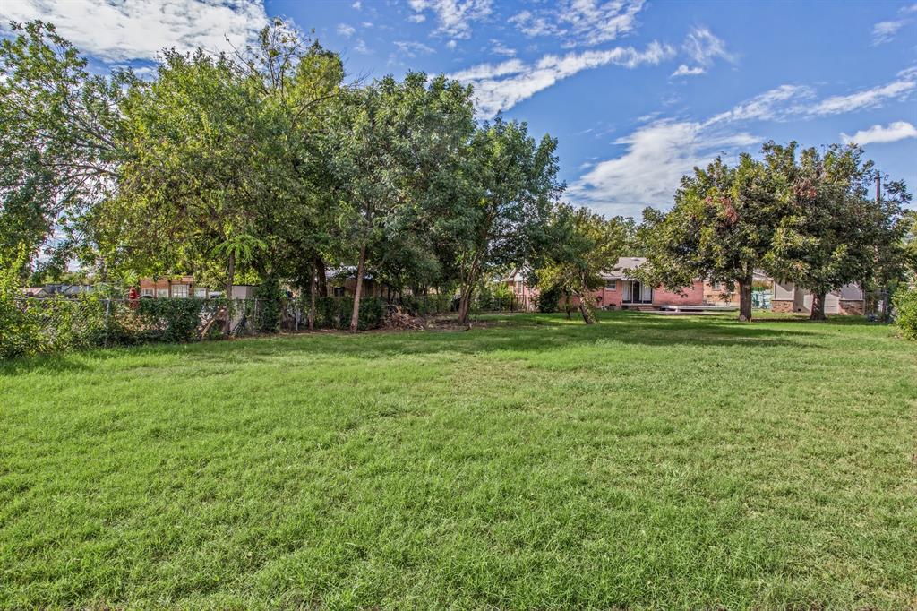 Expansive backyard featuring a large grass lawn, mature trees, and perimeter chain-link fencing