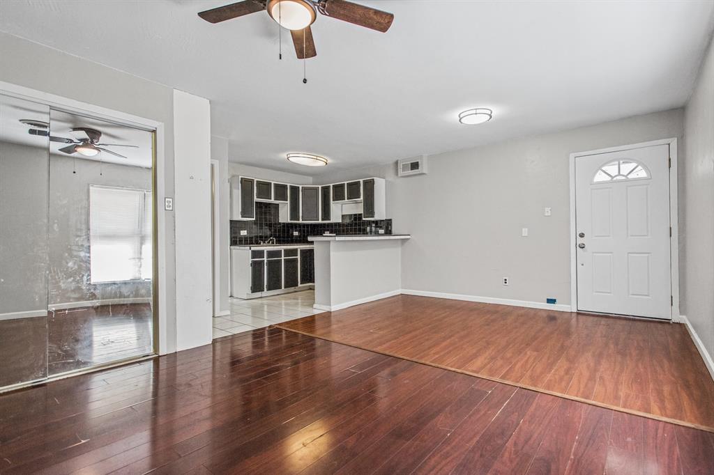 Living area featuring wood-finish flooring, ceiling-mounted lighting, and mirrored closet doors, with a kitchen island and tile backsplash