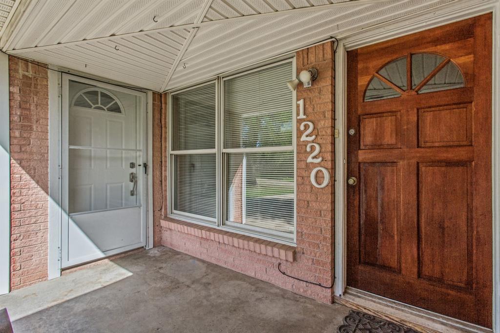 Covered entryway featuring a brick facade, solid wood entry door with a semi-circular transom window, secondary storm door, and large multi-pane windows Covered entryway featuring a brick facade, solid wood entry door with a semi-circular transom window, secondary storm door, and large multi-pane windows