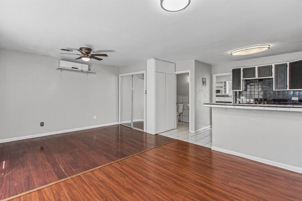 Wood-finish flooring, wall-mounted ductless air conditioning unit, ceiling fan, mirrored closet doors, and tile-topped breakfast bar