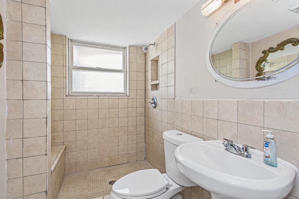 Full-tile shower surround with built-in wall niche, pedestal sink, chrome hardware, oval vanity mirror, and window providing natural illumination