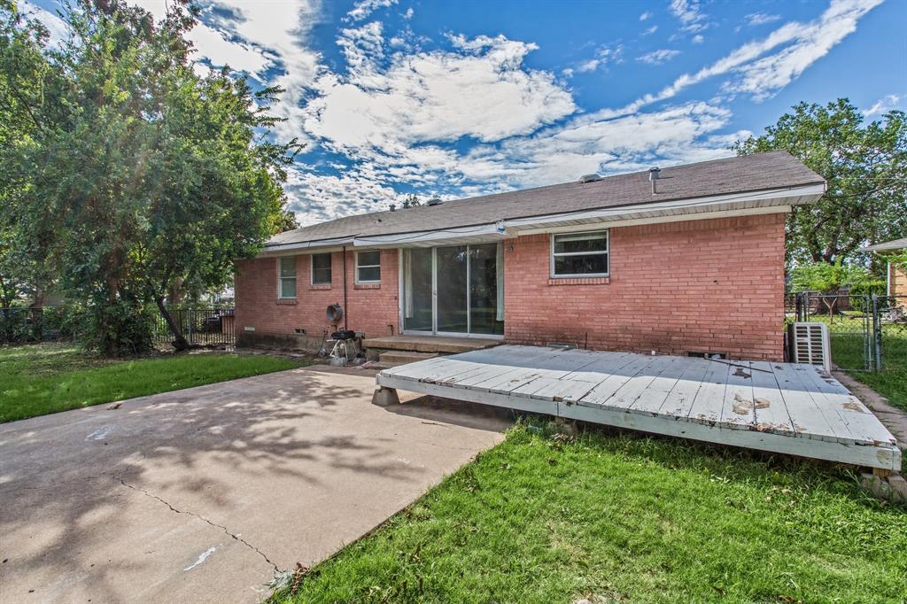 Exterior red brick facade featuring a sliding glass door, elevated wood deck, concrete patio, and fenced backyard with mature trees