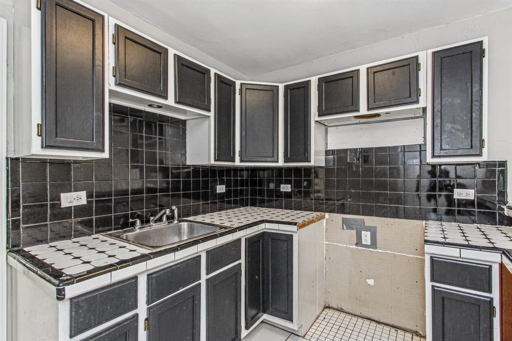 Kitchen featuring dark-finish shaker cabinetry, patterned tile countertops, black tiled backsplash, and a stainless steel undermount sink