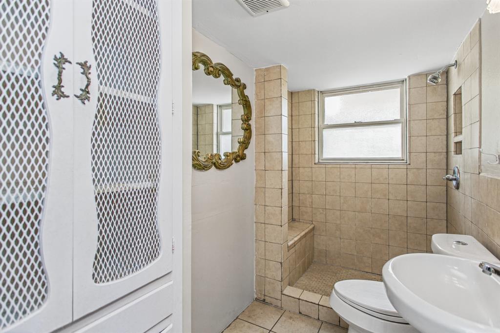 Bathroom featuring a walk-in tile shower with an integrated bench, built-in floor-to-ceiling storage cabinetry with wire mesh door panels, and neutral-toned wall and floor tiling
