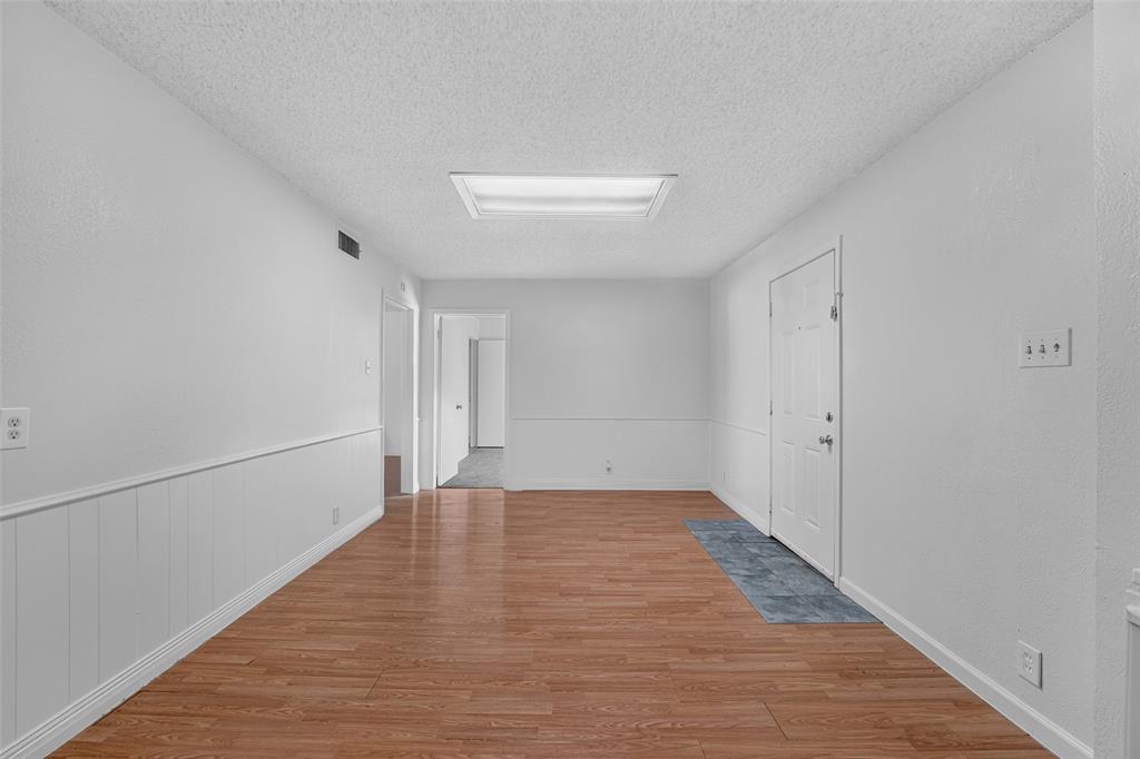 Interior space featuring wood-finish flooring, wainscoting, recessed ceiling lighting, and a six-panel door Interior space featuring wood-finish flooring, wainscoting, recessed ceiling lighting, and a six-panel door