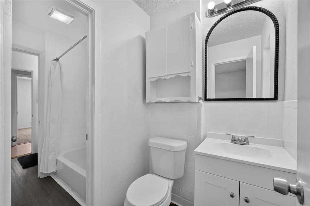 Bathroom featuring a vanity with integrated sink, arched wall mirror, wall-mounted storage cabinet, and a shower-tub combination with tile surround Bathroom featuring a vanity with integrated sink, arched wall mirror, wall-mounted storage cabinet, and a shower-tub combination with tile surround