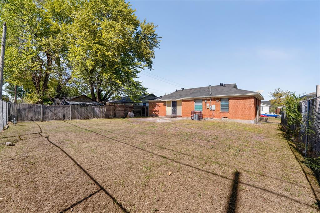 Expansive backyard featuring a brick exterior, wood privacy fencing, mature trees, and a ground-level concrete patio