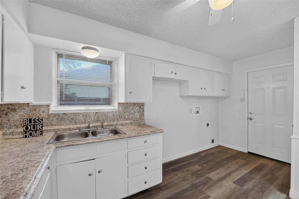 Kitchen featuring white cabinetry, stone-finish countertops, a double-basin stainless steel sink, wood-finish flooring, and a ceiling-mounted light fixture Kitchen featuring white cabinetry, stone-finish countertops, a double-basin stainless steel sink, wood-finish flooring, and a ceiling-mounted light fixture