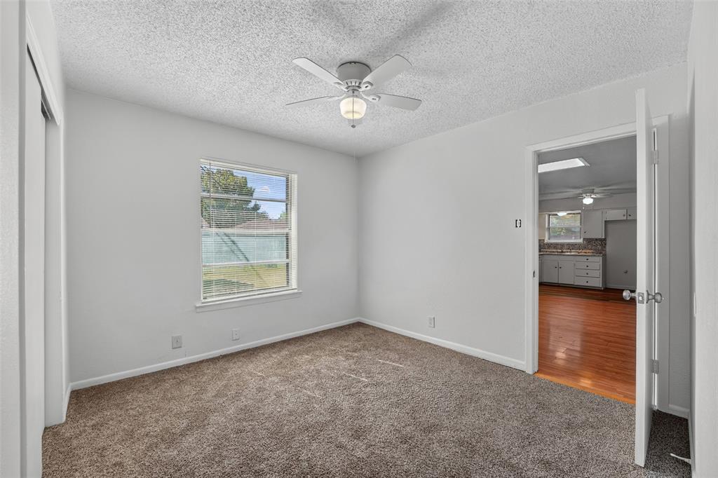 Interior room featuring neutral carpeting, a ceiling-mounted fan with integrated light fixture, a single-pane window, and a sliding closet door Interior room featuring neutral carpeting, a ceiling-mounted fan with integrated light fixture, a single-pane window, and a sliding closet door