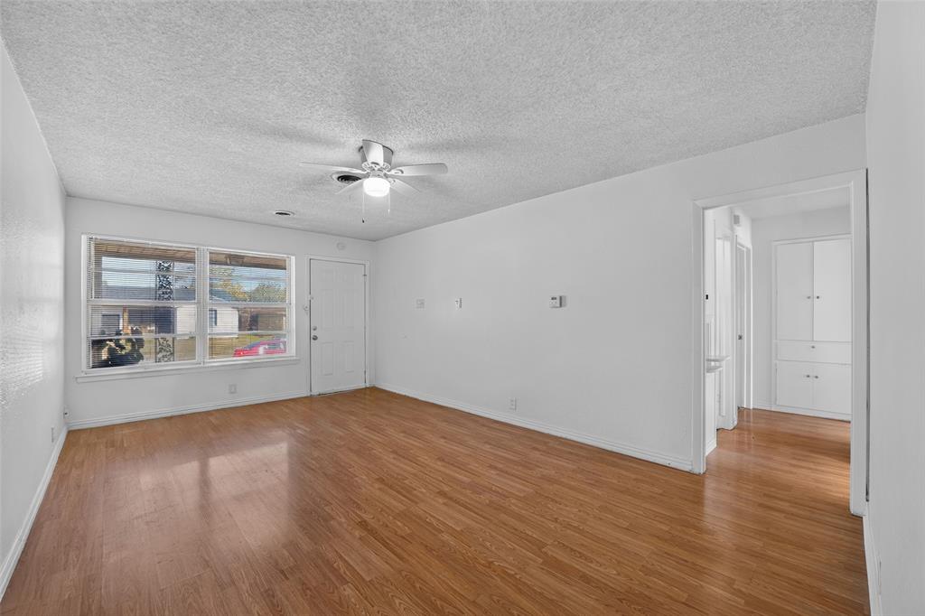 Living area featuring wood-finish flooring, a ceiling fan with integrated light, a large multi-pane window, and built-in cabinetry Living area featuring wood-finish flooring, a ceiling fan with integrated light, a large multi-pane window, and built-in cabinetry