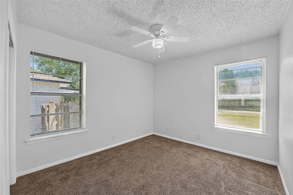 Neutral wall-to-wall carpeting, two dual-pane windows with horizontal blinds, and a white ceiling-mounted fan with light fixture