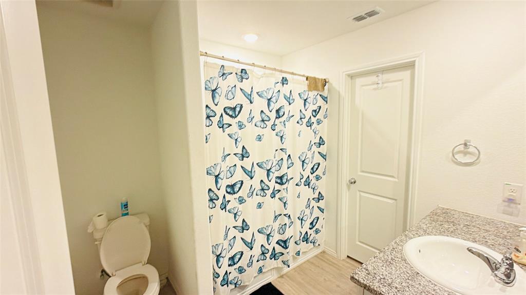 Bathroom featuring a vanity with a stone-finish countertop, undermount sink, chrome faucet, and wood-finish flooring