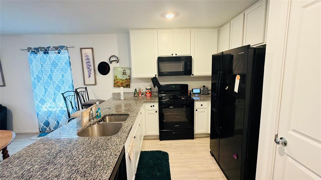 Kitchen featuring white cabinetry, stone-surface countertops, dual basin stainless steel sink, and built-in black appliances